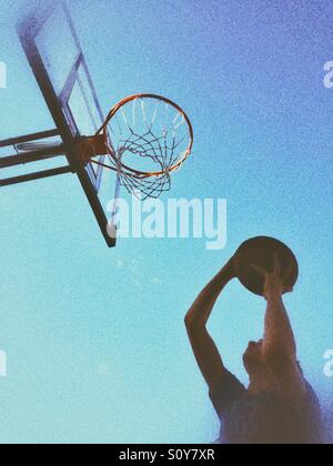 Teenage boy shooting a basketball. Outdoors shot, natural light, grainy edit. Stock Photo