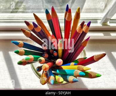 Colored pencils in a glass jar on a sunny window sill create a vibrant radial pattern Stock Photo