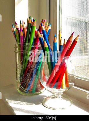 An assortment of colored pencils in glass containers sits on a sunny window sill Stock Photo