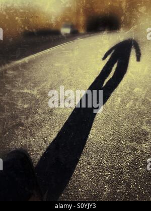 The long shadow of a man walking down a road. Stock Photo