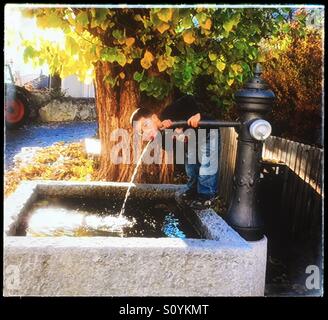 Young boy drinking from the water fountain well in the country in France Stock Photo