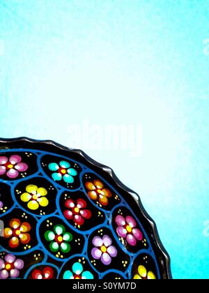 Vibrant hand painted flowers on decorative dish on blue background Stock Photo