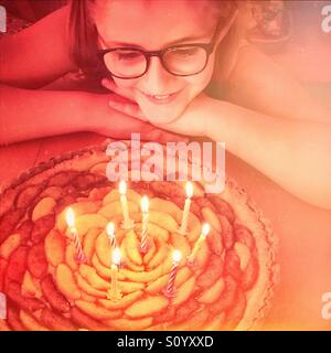 Little girl with eyeglasses looking at her birthday apple pie with 8 candles Stock Photo