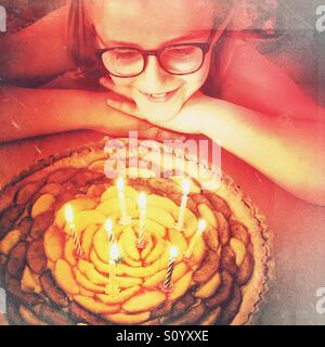 Little girl with eyeglasses looking at her birthday apple pie with 8 candles Stock Photo