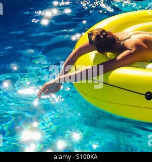 Woman sunbathing on a floating mat in blue waters. Stock Photo