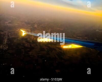 Plane at sunset, from a window seat on a regular commercial flight. Approaching dusk. Remains of a day. Stock Photo