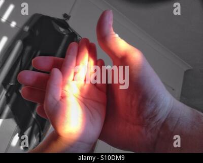 An adult male hand and a young child's hand in a beam of evening sunlight. Stock Photo