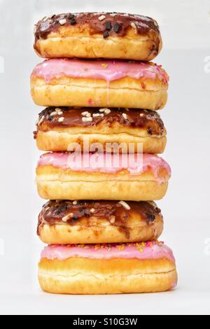 A tall stack of doughnuts with chocolate and pink icing on an isolated white background. Stock Photo