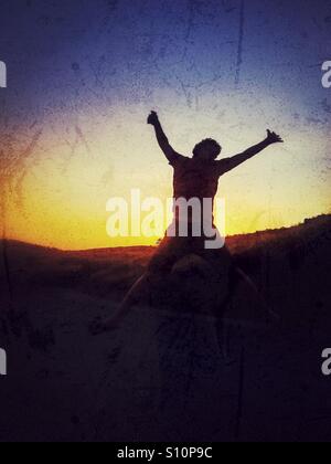Jumpin for joy. Young man jumping up in the air backlit by the warm lights of sunset. Stock Photo