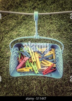 Plastic clothes pegs in a basket suspended to a clothes line. Stock Photo