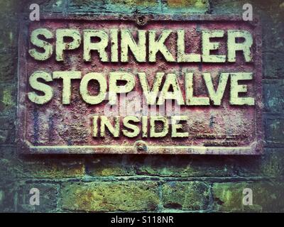 Sprinkler stop valve inside sign on brick wall Stock Photo