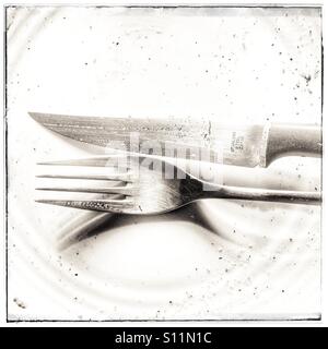 Knife and fork on plate after meal. Stock Photo