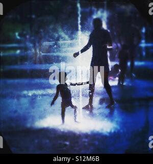 Father and son playing in a fountain in the summer heat Stock Photo