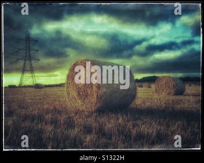A Grunge Effect Picture of Hay Bales in a field in the Cotswold Region of England. The sun is setting behind a large Electricity Pylon Tower. Photo Credit - © COLIN HOSKINS. Stock Photo