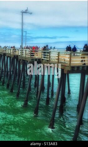 People on pier fishing, walking...pelican on top light pole Stock Photo