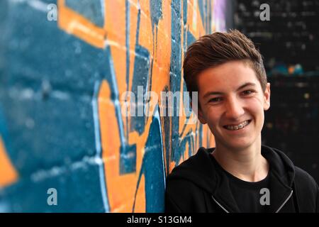 Teenager leaning against graffiti wall Stock Photo