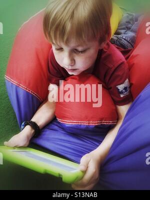 A boy lying on his stomach on a deflated ball plays on his mobile device. Stock Photo