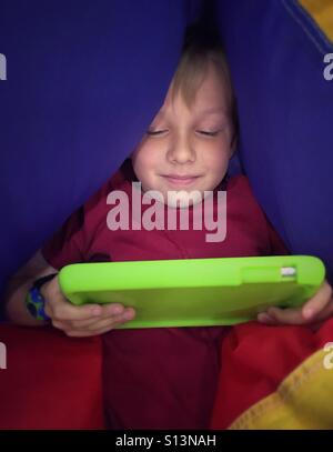 A boy snuggled into a partially deflated ball plays on his mobile device. Stock Photo