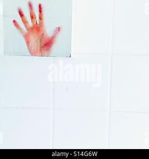 Hands Up !  A hand reflected in a bathroom mirror on white tiles Stock Photo