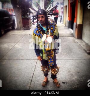 A Mexican dressed as an Aztec dancer plays music in the street in Colonia Roma, Mexico City, Mexico Stock Photo