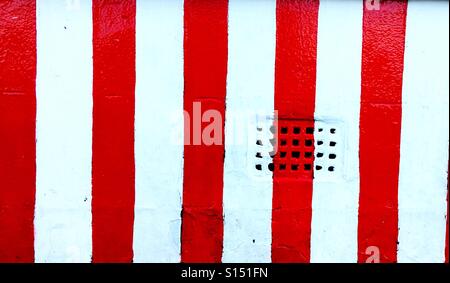Red and white stripes painted on a wall with ventilation brick Stock Photo