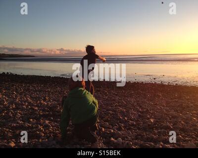 Two kids playing at throwing stones on a beach at sunset Stock Photo