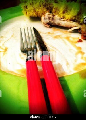 A knife and fork on a dirty plate at the end of a meal. Stock Photo