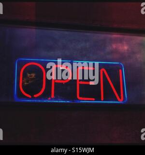 A glowing red neon open sign beckons from a window in the evening. Stock Photo