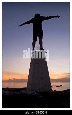 Watching the sun set over the Worms Headland at Rhossili Bay on the Gower Peninsula near Swansea from the trig point on top of Rhossili Downs. Stock Photo