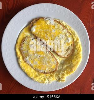 Scrambled eggs over toasts on white plate and wooden surface. Stock Photo