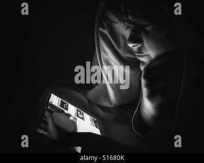 Teenager using an iPad at night, under duvet Stock Photo