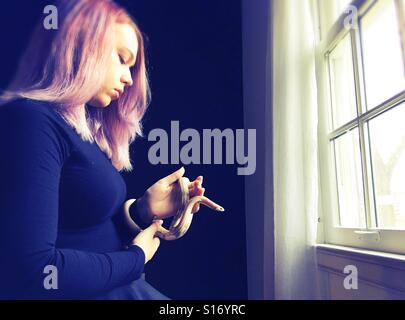 A teenage girl holding a snake next to a window. Stock Photo