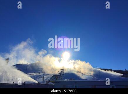Preparing the ski hill - making snow with bright sun and lens flare in the background Stock Photo