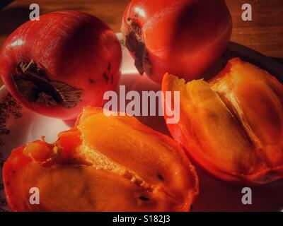 Persimmons on a plate, one cut in half, ready to eat Stock Photo