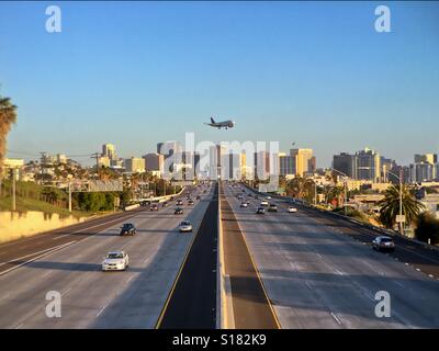 Plane flying over a city freeway with city skyline in the background. Interstate 5, San Diego, California, USA. Taken 2 April 2016. Stock Photo