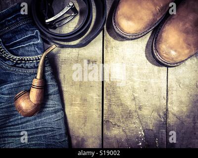 Wooden smoking pipe, leather boots and blue jeans on the wooden background, vintage toning Stock Photo