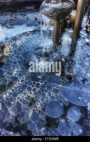 Bubbles formed by a fountain under thick ice on a garden pond in winter Stock Photo