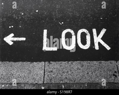 Look left sign. The word 'look' painted on the street in bold white capital letters, with arrow pointing to the left. Stock Photo