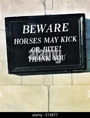 Funny sign with the words 'BEWARE HORSES MAY KICK OR BITE! THANK YOU' written in white capital letters. Stock Photo