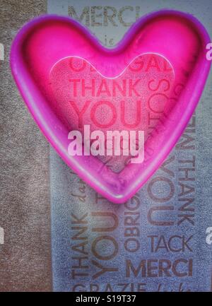 Pink plastic heart shaped cookie cutter on a background of the word Thank you in different languages Stock Photo