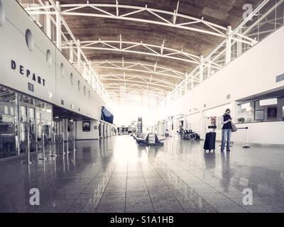 Lone woman using phone in an otherwise deserted departure lounge at airport Stock Photo