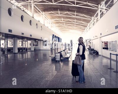 Lone woman with luggage standing in a deserted departure lounge at small airport Stock Photo