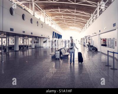 Lone woman with luggage standing in a deserted departure lounge at small airport Stock Photo