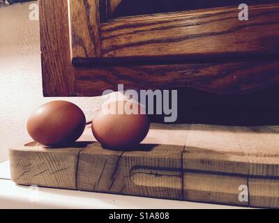 Two brown chicken eggs on a wooden cutting board in an old kitchen. Cracked wood on the cutting board shows it's age. Cooking and baking items. Stock Photo