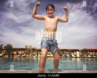An 11-year-old boy flexes his muscles after climbing out of a cold outdoor swimming pool while on holiday in Marrakech, Morocco. Stock Photo