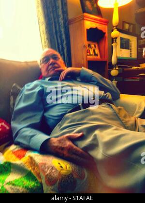 An older gentleman relaxing on a sofa watching TV. Stock Photo