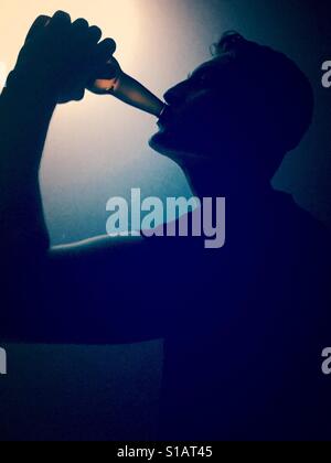Silhouette of a young man drinking from a glass bottle. Stock Photo