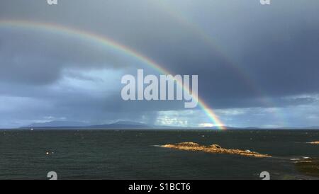 Double rainbow over the ocean with blue cloudy sky Stock Photo