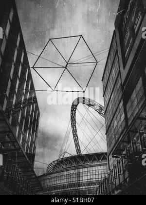 Black and white photo of a geometric cube sculpture in front of Wembley Stadium, seen between the buildings of the London Designer Outlet, London, England, UK. Stock Photo