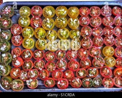 Variety of small tomatoes cut in half, topped with garlic, ready to be roasted. Stock Photo